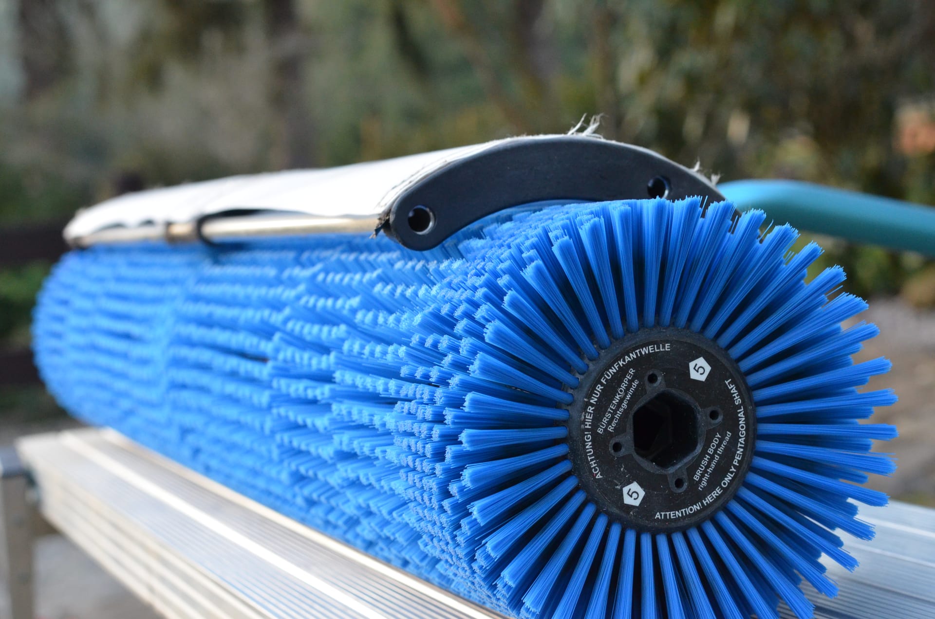 Close-up of a rotary brush head with blue radial bristles and a water feed tube