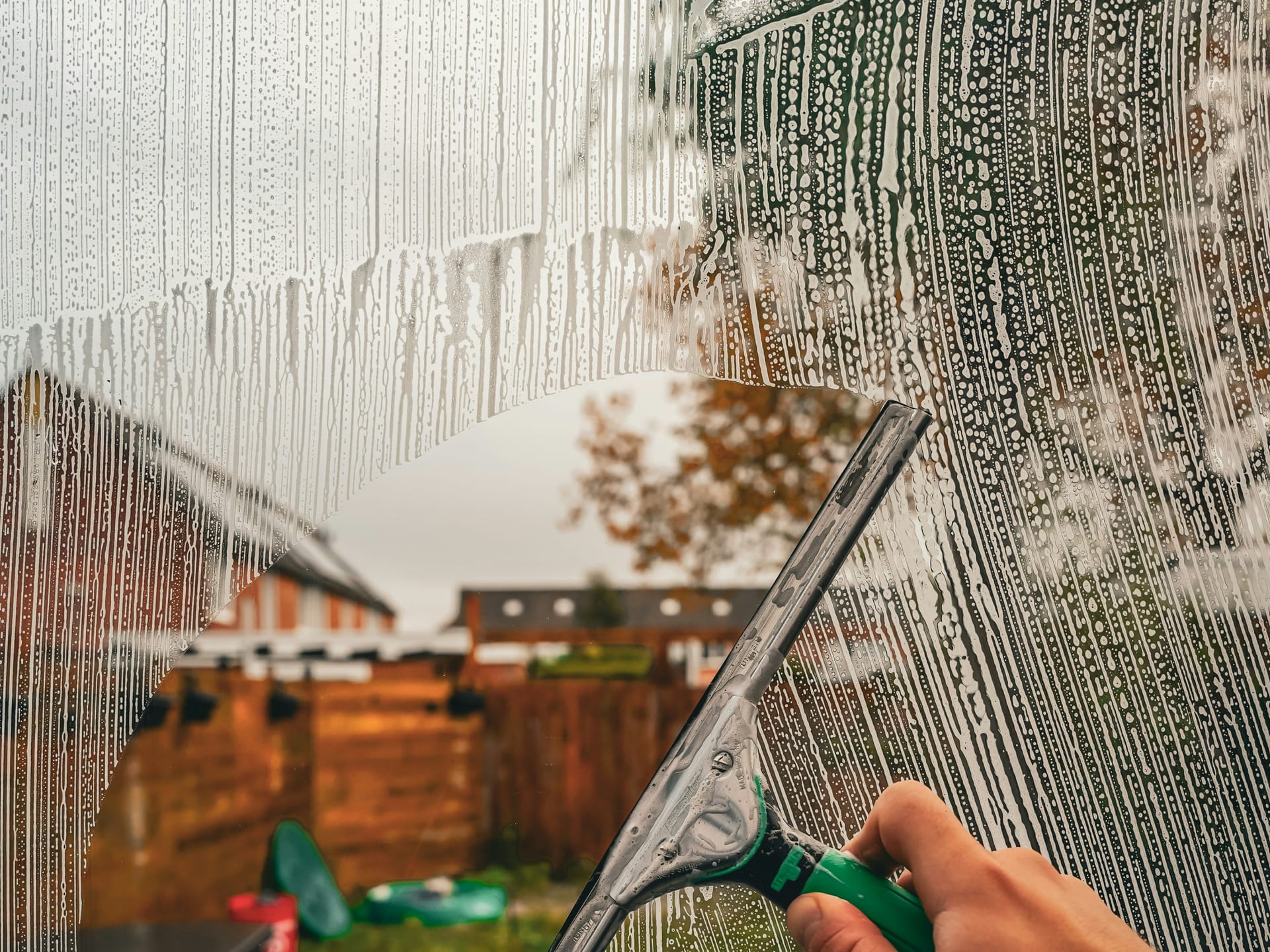 A squeegee pulling through soapy glass and leaving a clean swipe