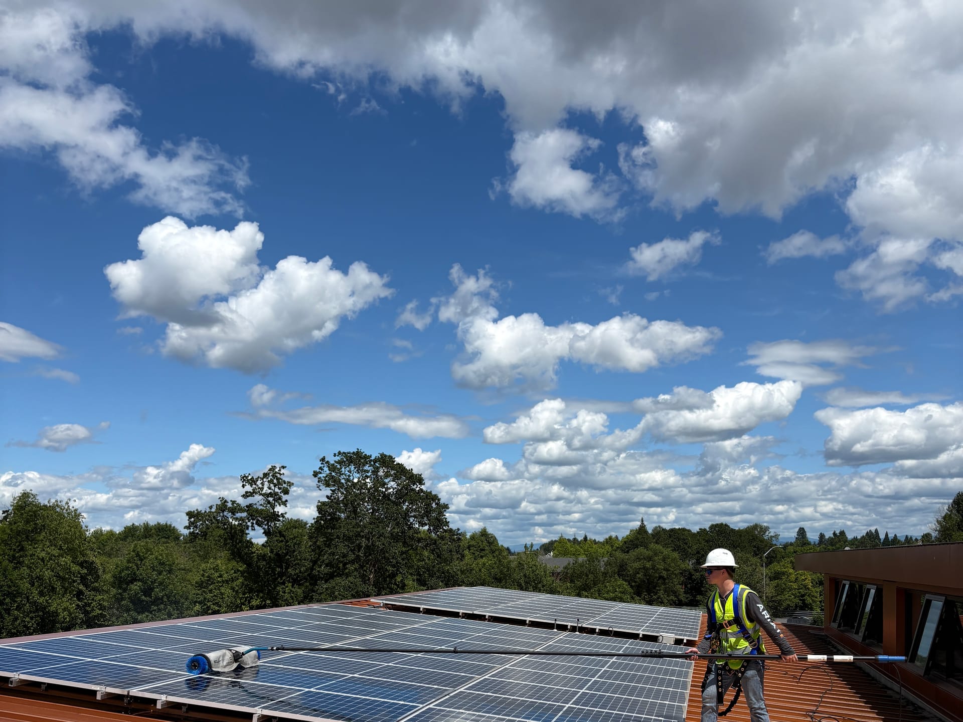 A technician cleaning a large commercial rooftop array with a water-fed pole and rotary brush