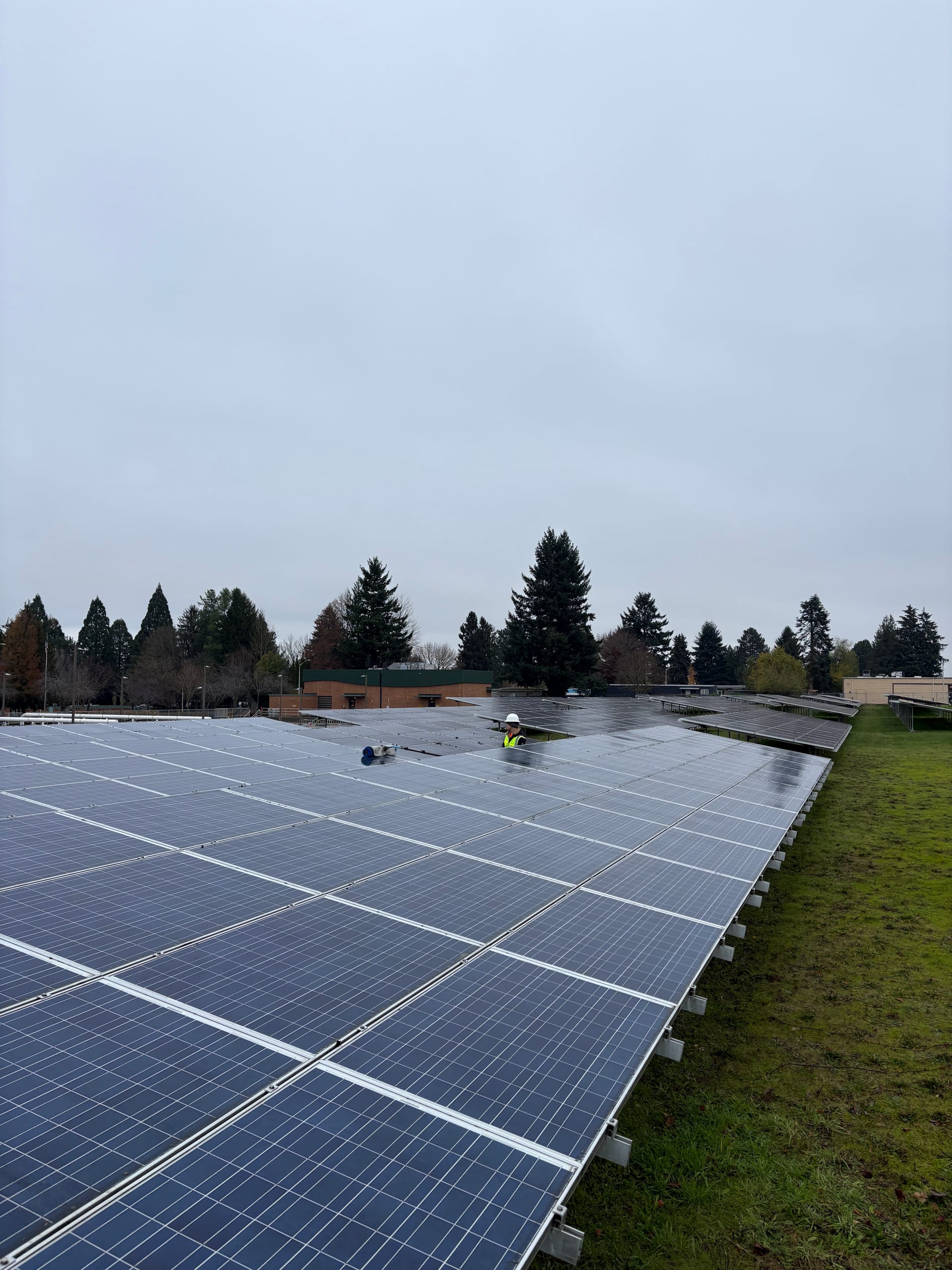 A technician in a hard hat and hi-vis vest working in a large ground-mount solar array