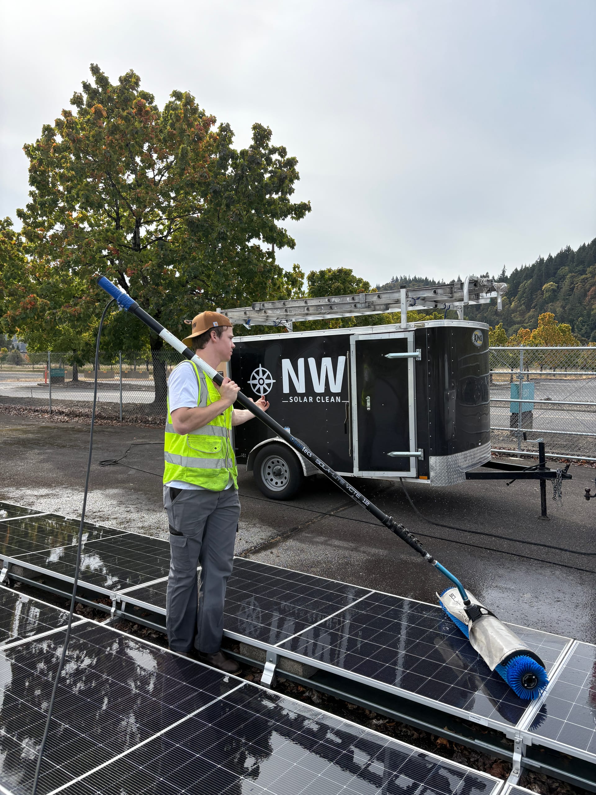 A technician cleaning ground-mount solar panels with the NW Solar Clean truck and trailer behind