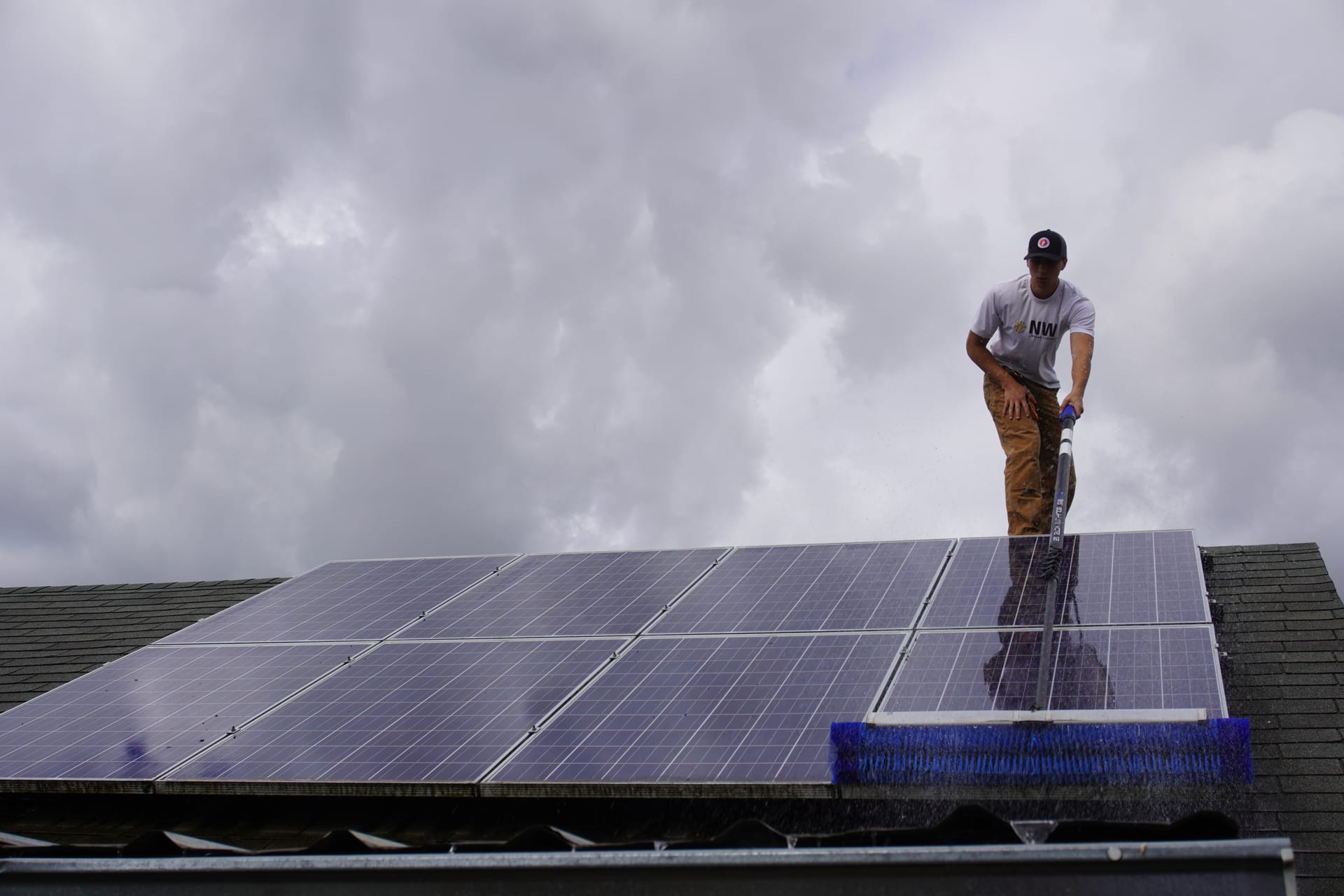 Technician cleaning residential rooftop solar panels with a water-fed rotating brush